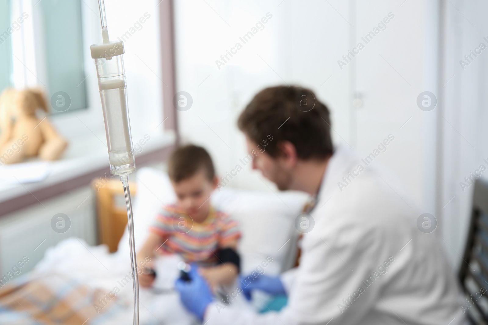 Photo of Doctor examining little child in hospital, focus drip chamber