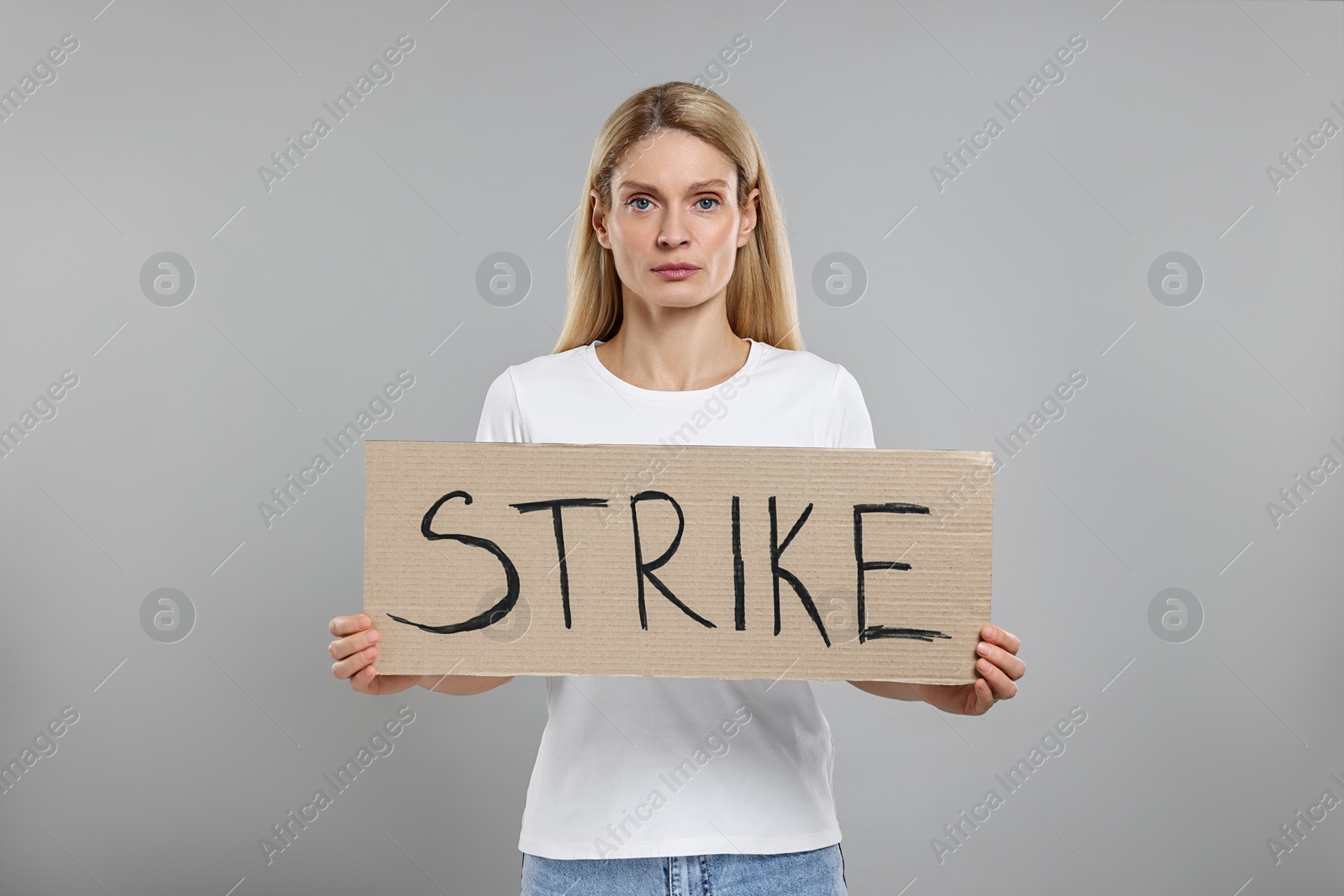 Photo of Woman holding cardboard banner with word Strike on grey background