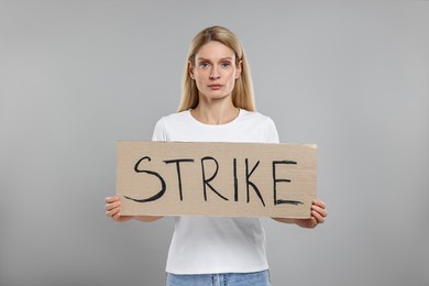 Woman holding cardboard banner with word Strike on grey background