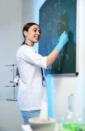 Photo of Female scientist writing chemical formula on chalkboard indoors