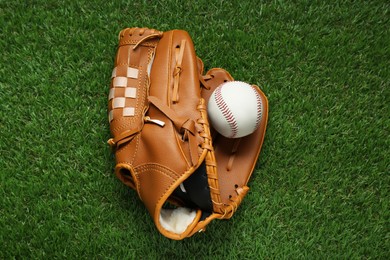 Photo of Catcher's mitt and baseball ball on green grass, top view. Sports game