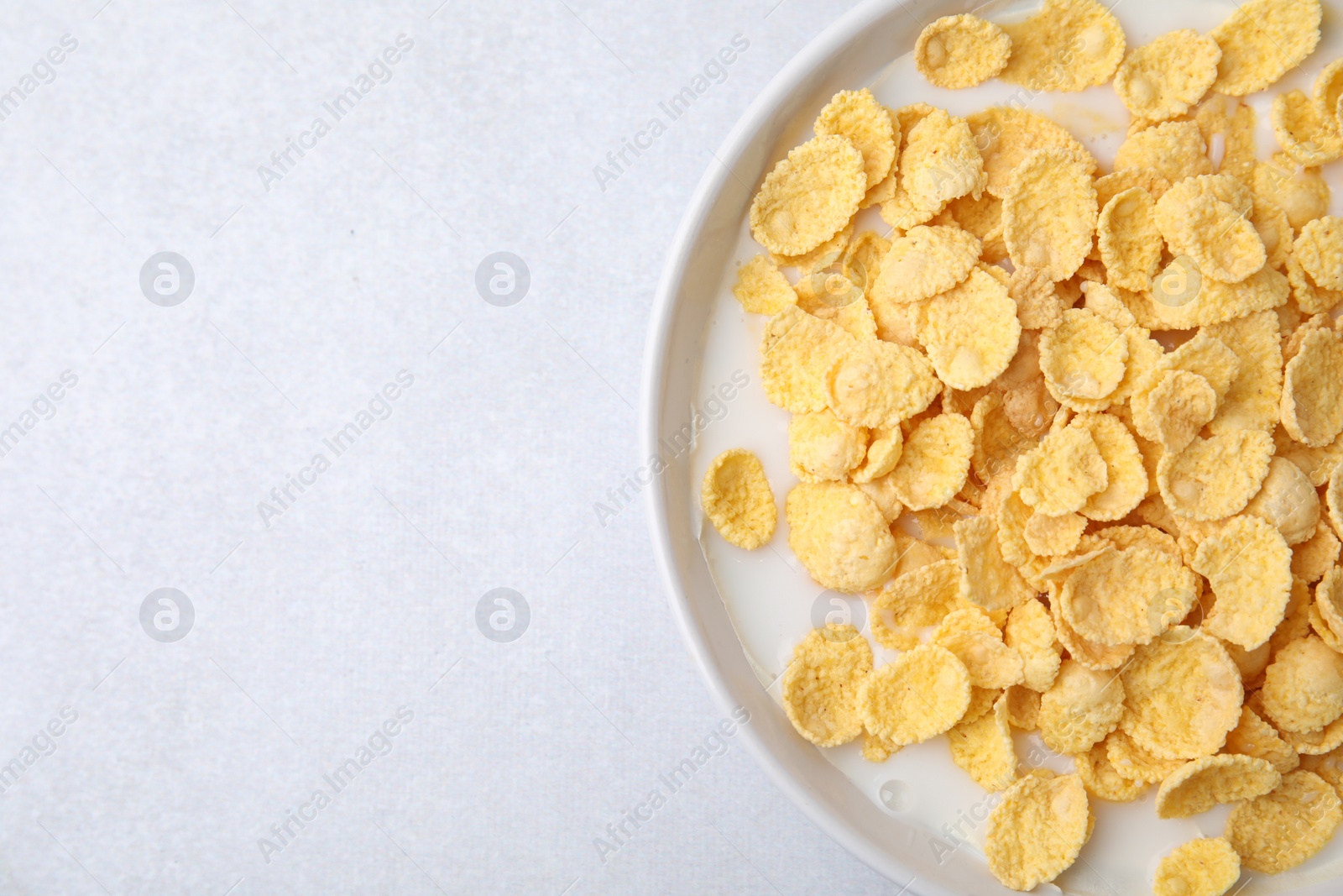 Photo of Breakfast cereal. Corn flakes and milk in bowl on light grey table, top view. Space for text