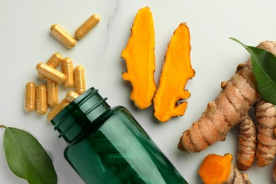 Photo of Turmeric roots, pills and bottle on white marble table, flat lay