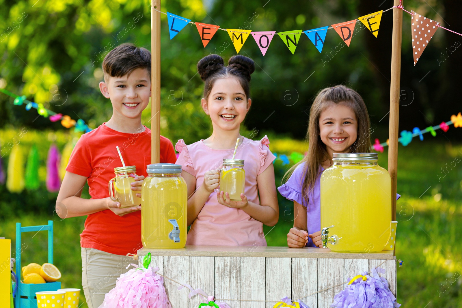 Photo of Cute little children at lemonade stand in park. Summer refreshing natural drink