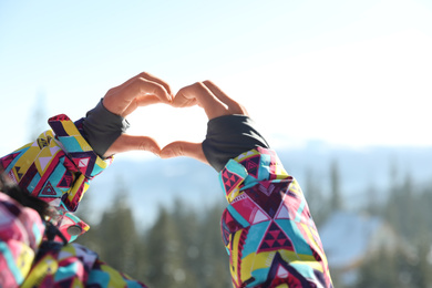 Photo of Woman making heart with her hands in mountains, closeup. Winter vacation
