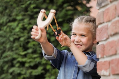 Photo of Little girl playing with slingshot outdoors. Kid's toy