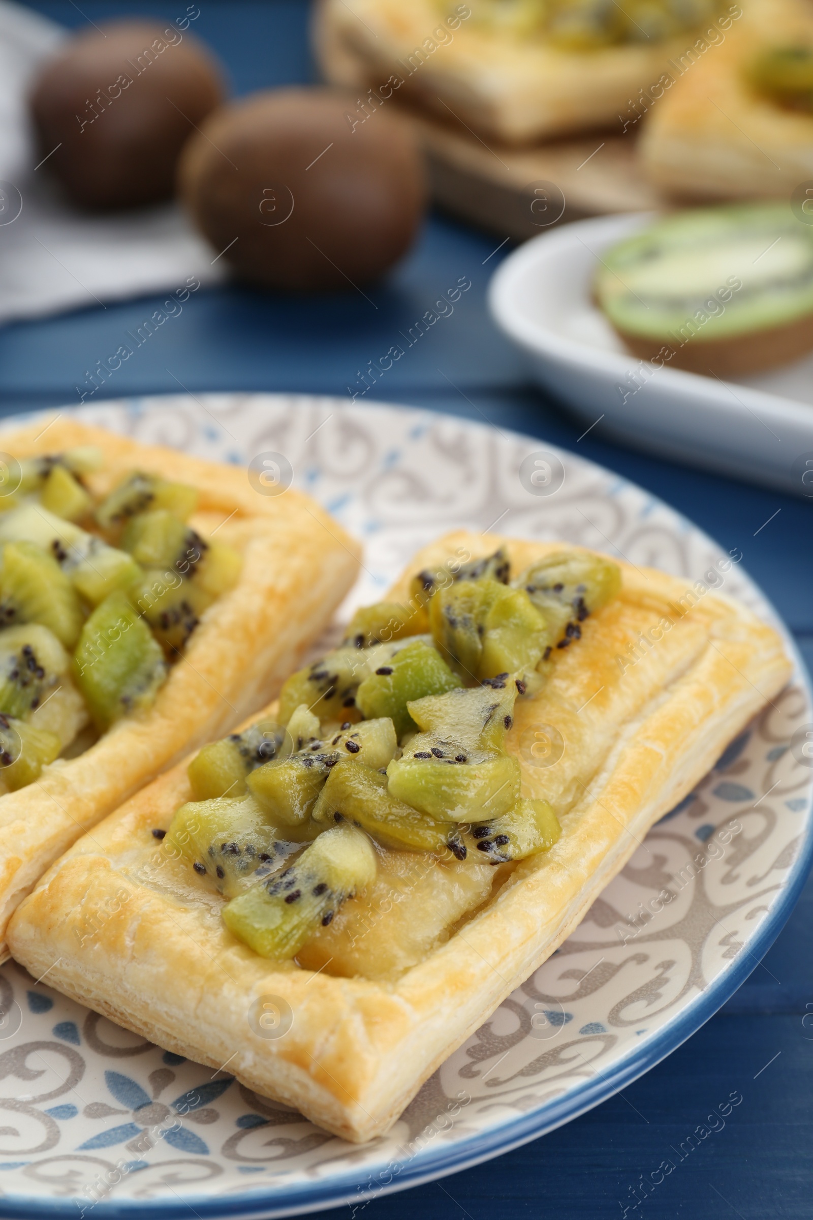 Photo of Fresh tasty puff pastry with kiwi on blue wooden table, closeup