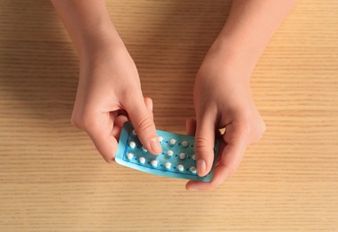 Photo of Woman taking oral contraception pill at wooden table, top view