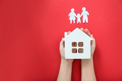 Photo of Child holding house model near silhouette of people on color background, top view
