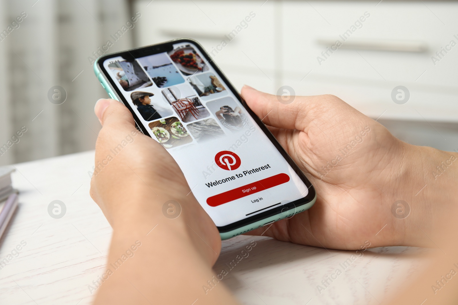 Photo of MYKOLAIV, UKRAINE - JULY 10, 2020: Woman holding Iphone 11 with Pinterest app on screen at table, closeup