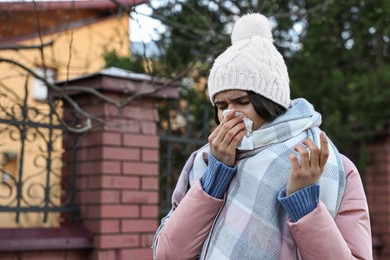 Woman with tissue blowing runny nose outdoors, space for text. Cold symptom