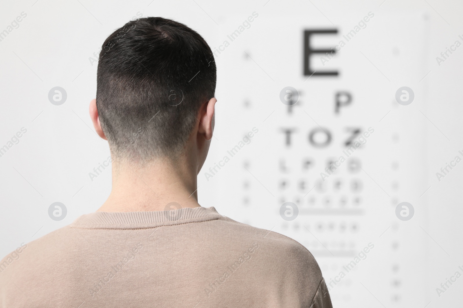 Photo of Eyesight examination. Young man looking at vision test chart indoors, back view