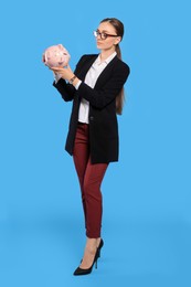 Sad young businesswoman with piggy bank on light blue background