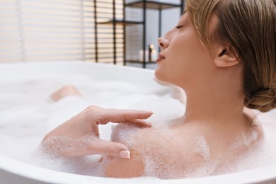 Photo of Beautiful woman taking bath with foam in tub indoors