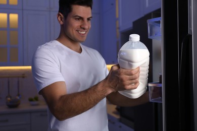Photo of Man holding gallon bottle of milk near refrigerator in kitchen at night