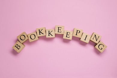 Photo of Word Bookkeeping made with wooden cubes on pink background, top view