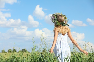 Photo of Young woman wearing wreath made of flowers in field on sunny day, back view