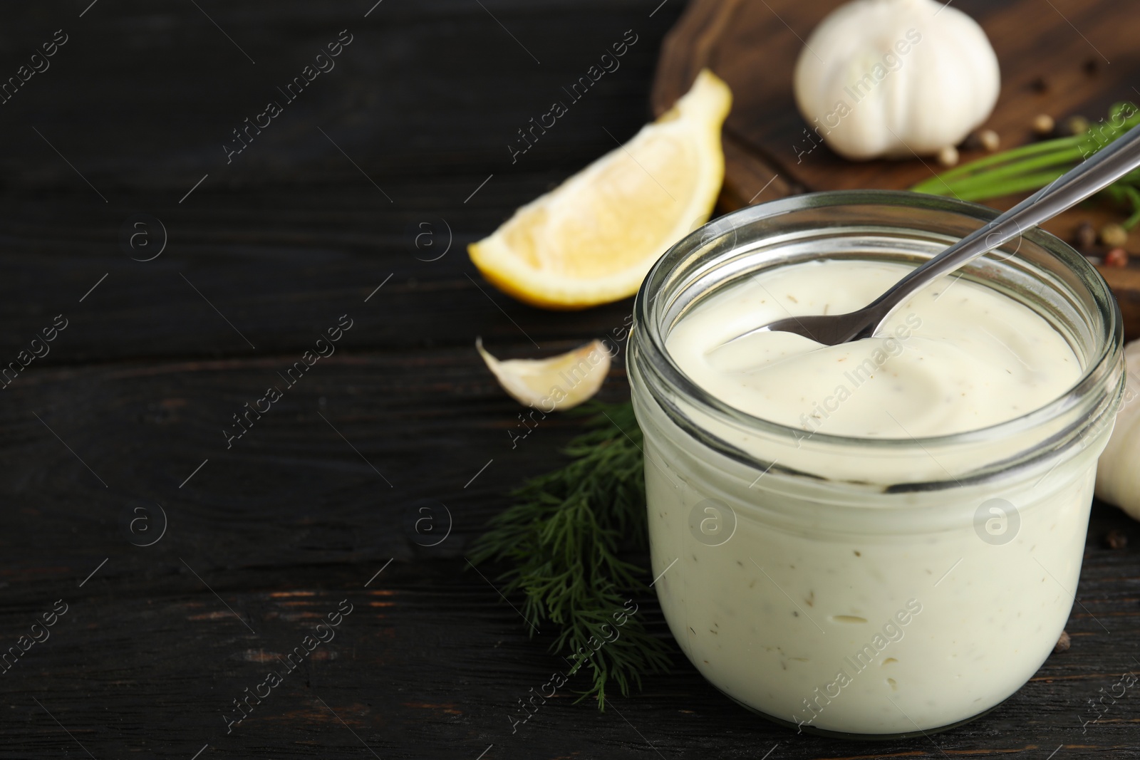 Photo of Composition with jar of garlic sauce on wooden table. Space for text