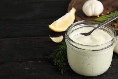 Photo of Composition with jar of garlic sauce on wooden table. Space for text