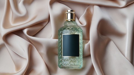 Photo of Luxury bottle of perfume on beige silk, top view