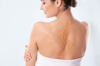 Young woman with natural scrub on her back against light background