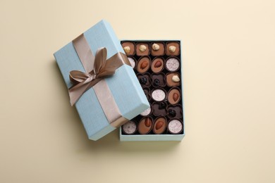 Photo of Open box of delicious chocolate candies on beige background, top view