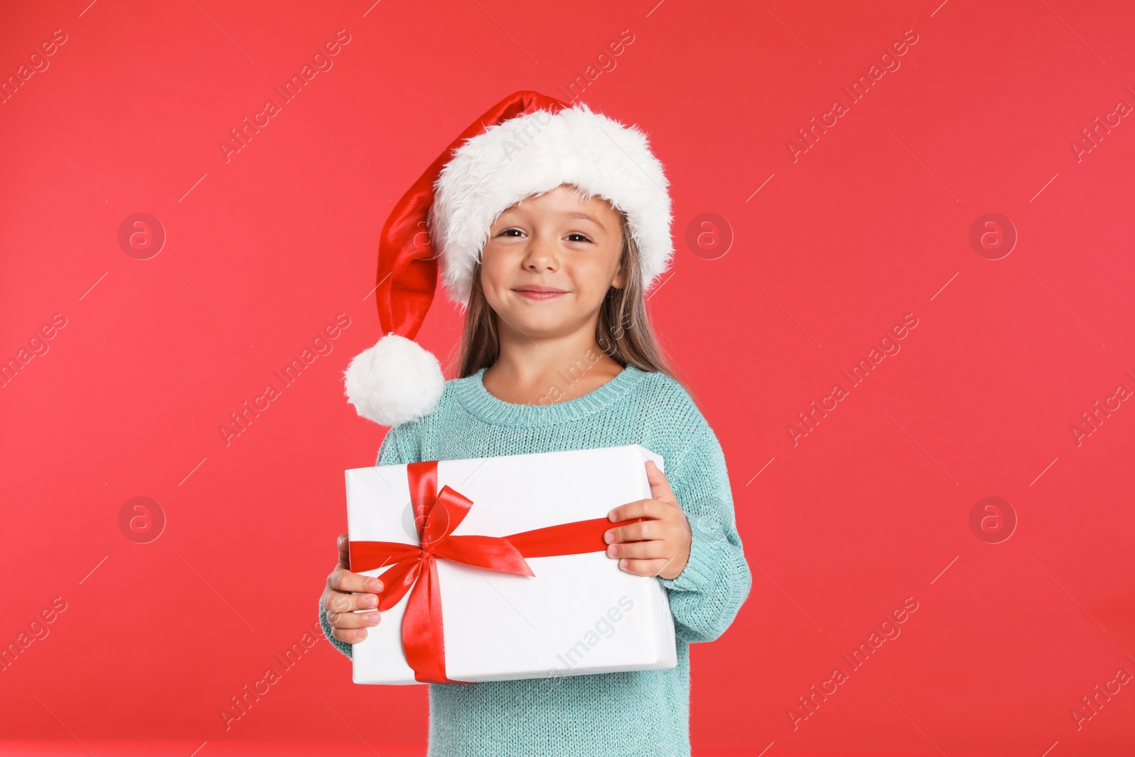 Photo of Happy little child in Santa hat with gift box on red background. Christmas celebration