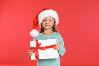 Happy little child in Santa hat with gift box on red background. Christmas celebration