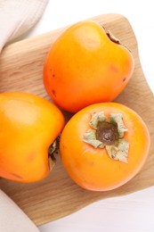 Board with delicious ripe persimmons on white wooden table, top view