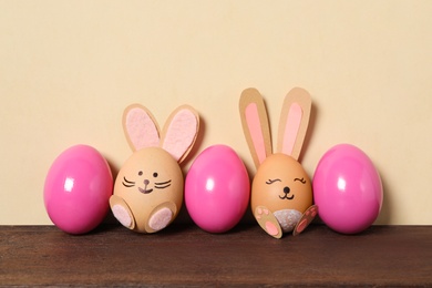 Two eggs as cute bunnies among others on wooden table against beige background. Easter celebration