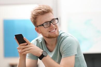 Photo of Portrait of handsome young man with glasses and smartphone in room