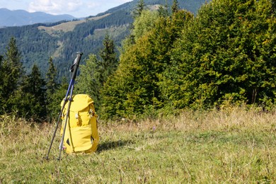 Photo of Yellow backpack and trekking poles outdoors on sunny day. Mountain tourism