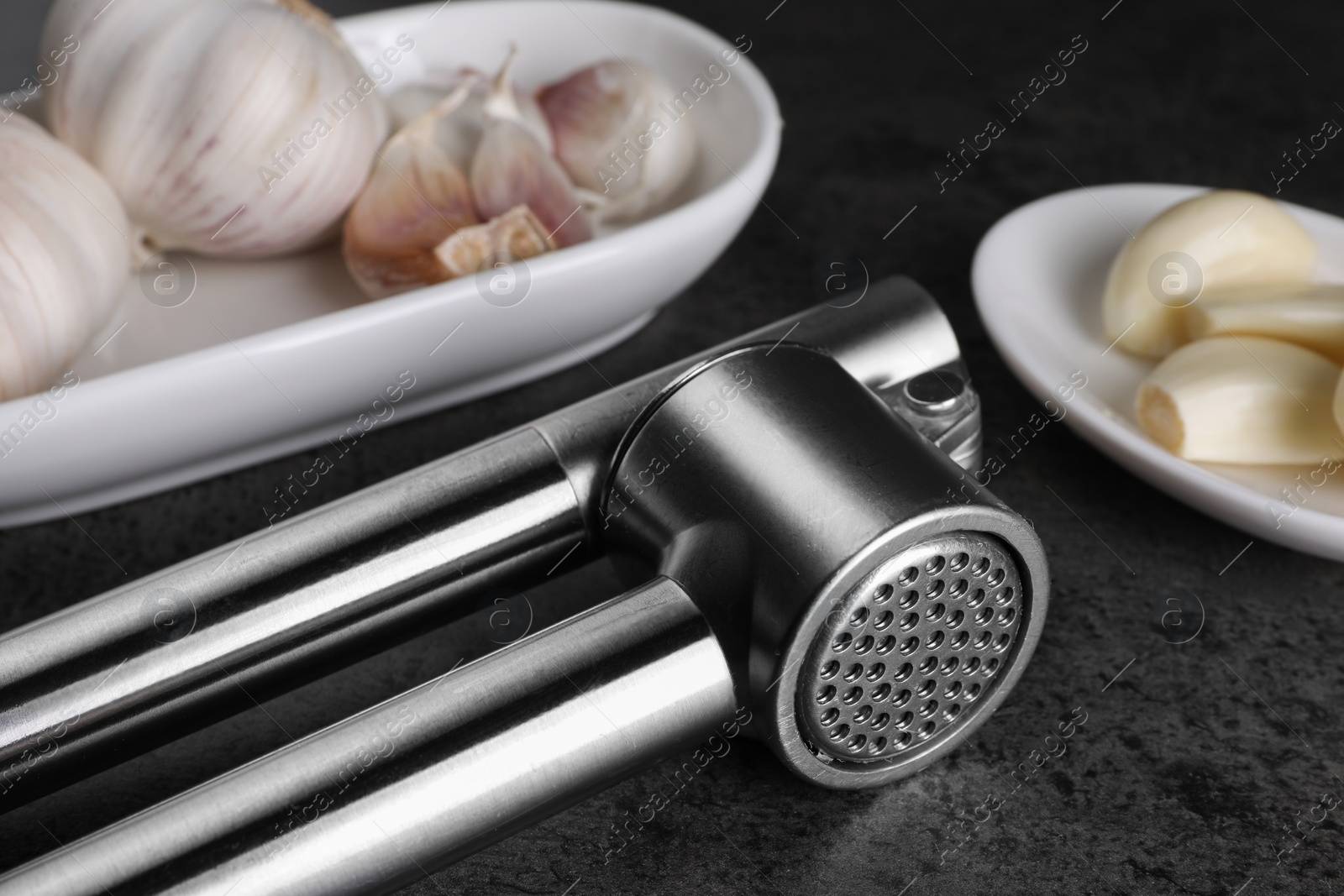 Photo of Garlic press with cloves and bulbs on grey table, closeup