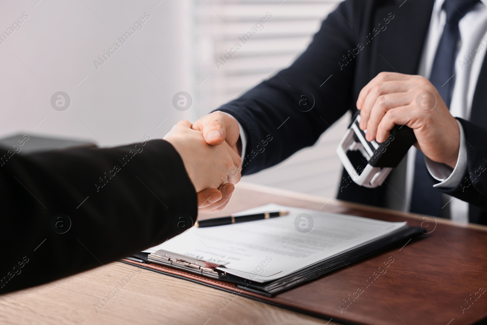 Photo of Notary shaking hands with client at wooden table in office, closeup