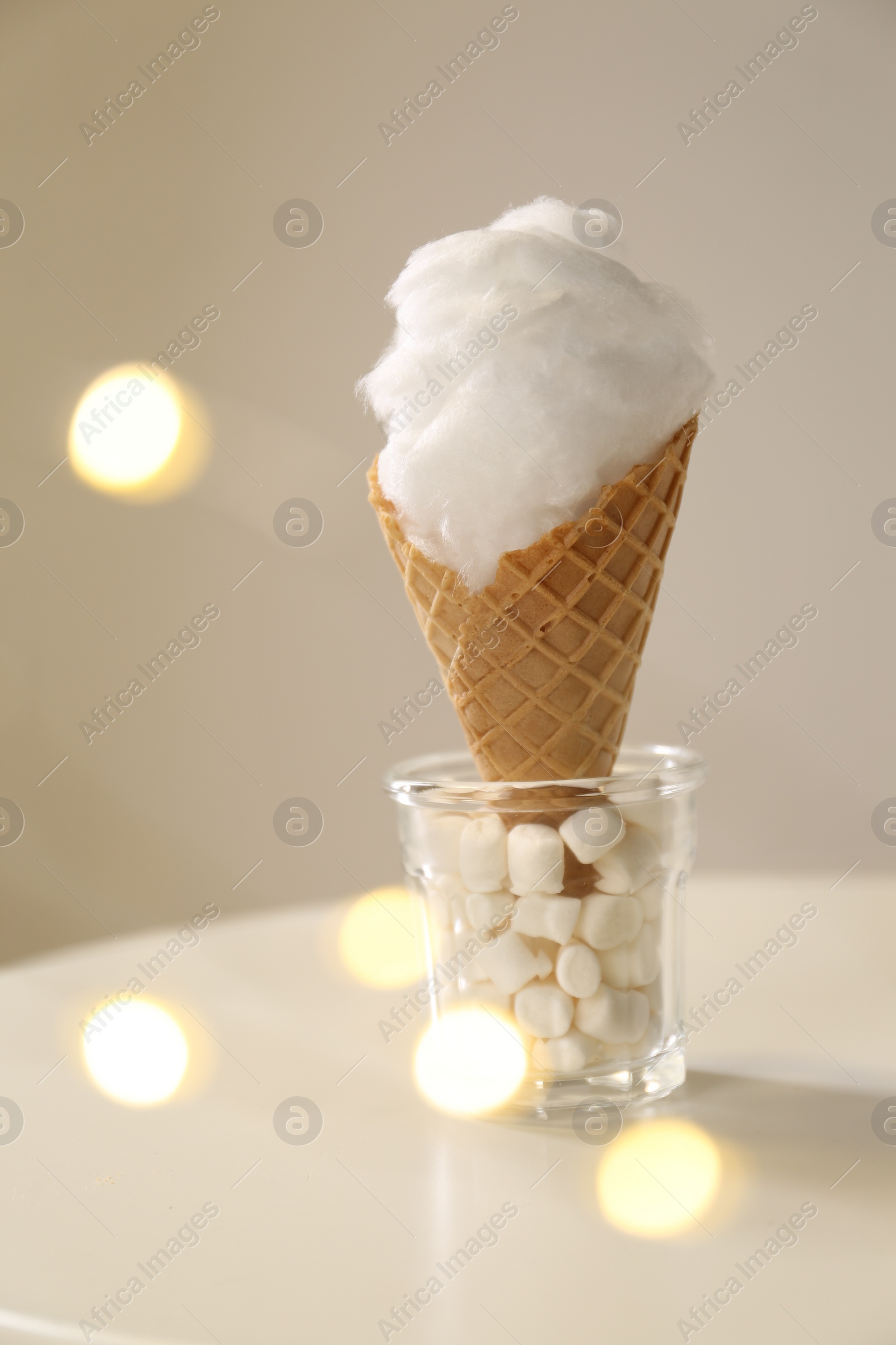 Photo of Sweet cotton candy in waffle cone on table against blurred lights