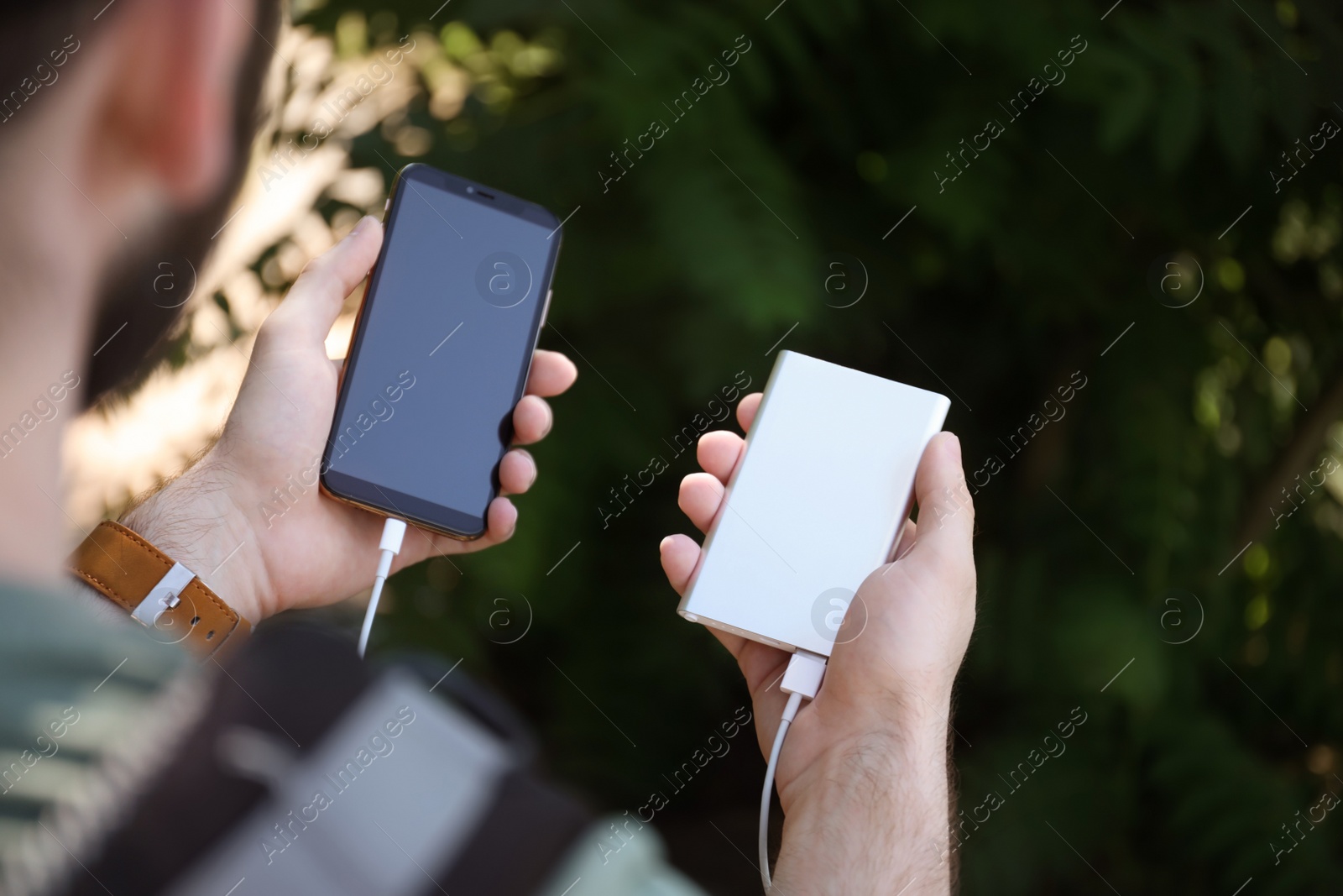 Photo of Man charging mobile phone with power bank in forest, closeup