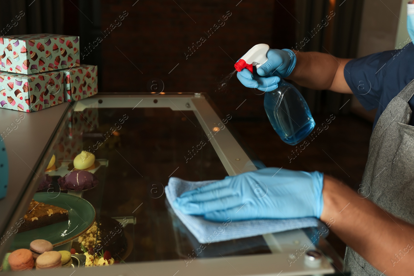 Photo of Worker in gloves disinfecting dessert showcase at cafe, closeup