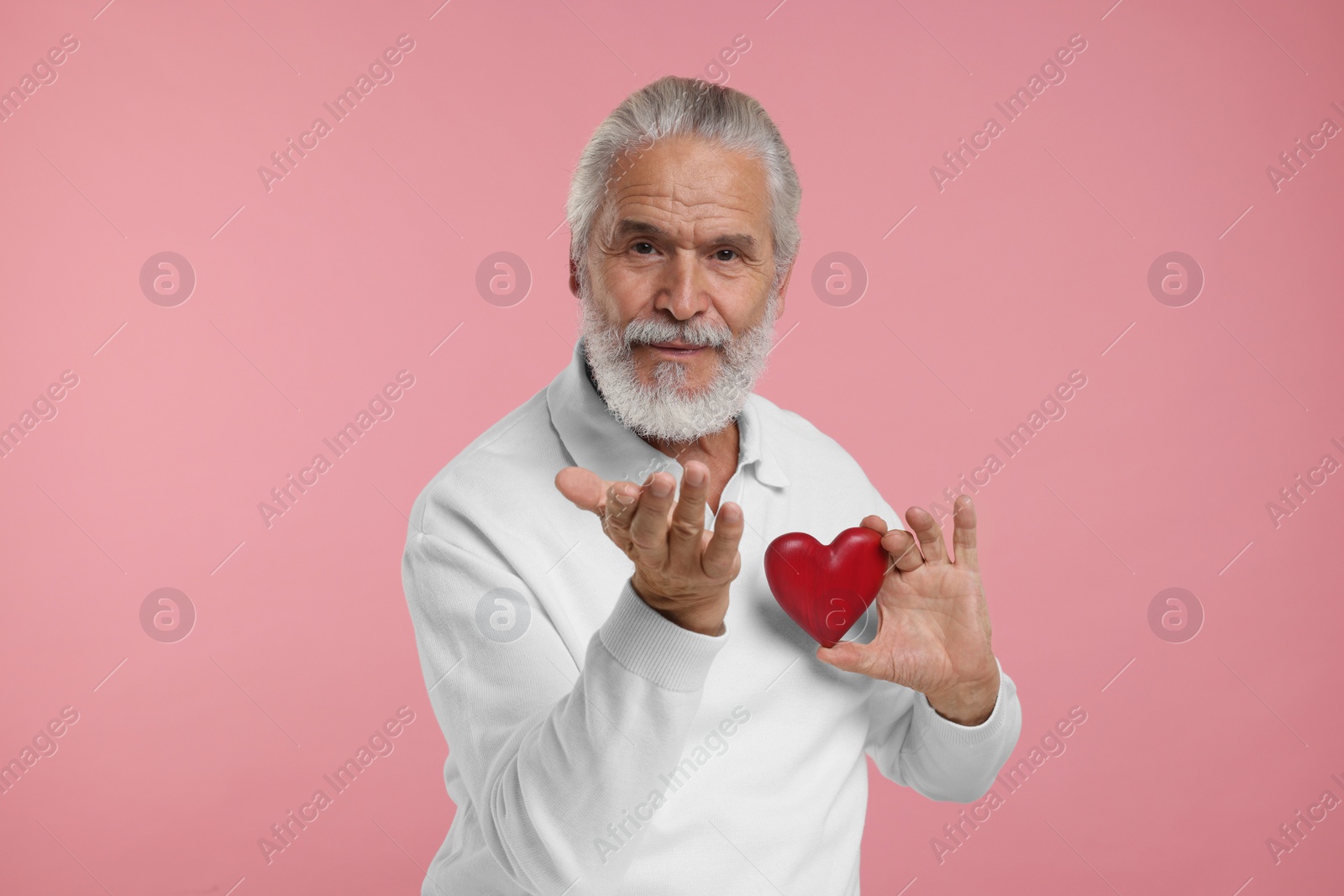 Photo of Senior man with red decorative heart on pink background