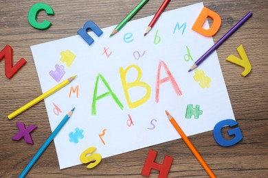 Photo of Sheet of paper with abbreviation ABA (Applied behavior analysis), plastic letters and pencils on wooden table, flat lay