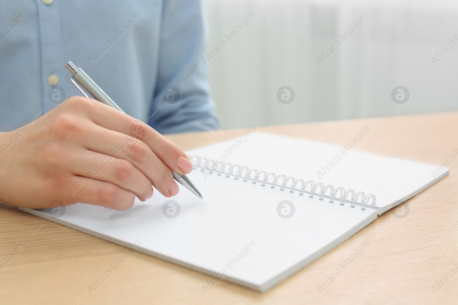 Photo of Woman writing in notebook at wooden table, closeup