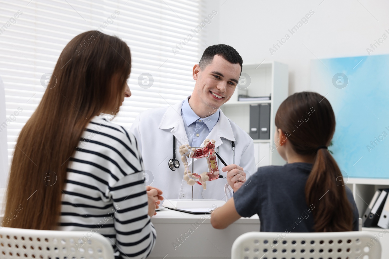Photo of Gastroenterologist with model of intestine consulting woman and her daughter in clinic