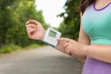 Young woman checking pulse with medical device after training in park, closeup