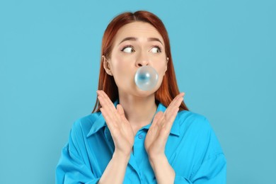 Photo of Surprised woman blowing bubble gum on turquoise background