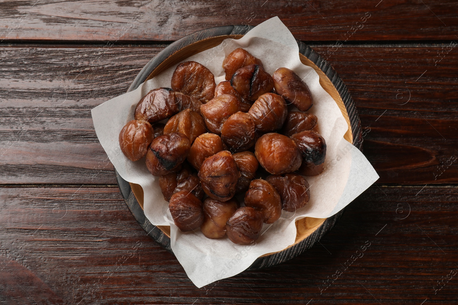 Photo of Roasted edible sweet chestnuts in bowl on wooden table, top view