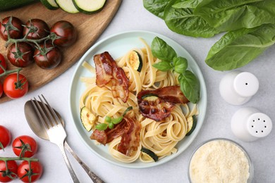 Tasty pasta with bacon and basil on light grey table, flat lay