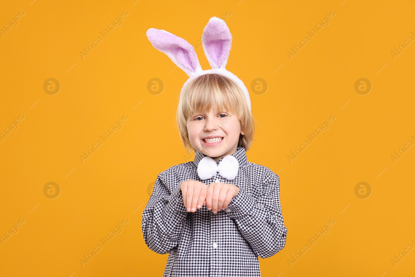 Photo of Happy boy wearing bunny ears headband on orange background. Easter celebration