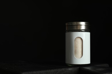 Photo of Salt shaker on wooden board against black background. Space for text