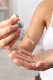 Woman applying cosmetic serum onto her hand on blurred background, closeup