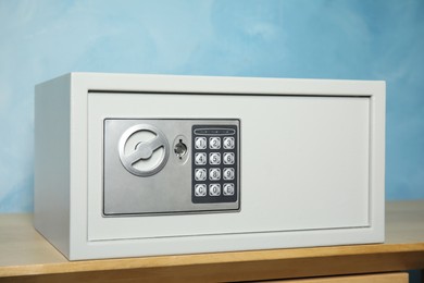 Closed steel safe on wooden table against light blue background