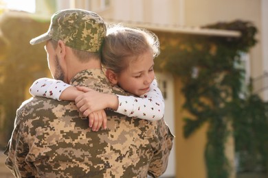 Photo of Soldier in Ukrainian military uniform hugging his daughter outdoors, space for text. Family reunion